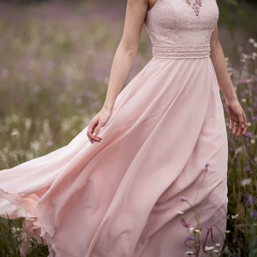 Dreamy blush wedding dress in pastel pink, with flowing chiffon and subtle lace details for an ethereal bridal look.