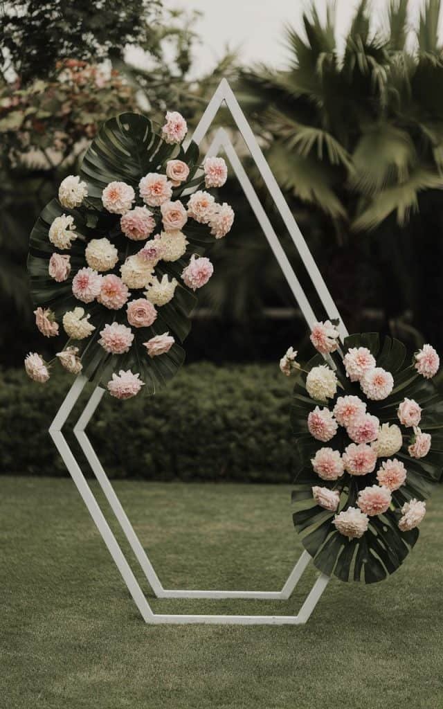 Stylish Wedding Arch Flowers featuring a geometric hexagonal arch with dahlias, roses, and greenery, ideal for couples seeking a modern, unique backdrop.
