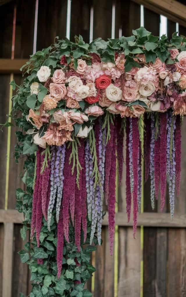 Charming winter Wedding Arch Flowers featuring vibrant red poinsettias and rich green evergreens, ideal for a holiday-themed wedding.
