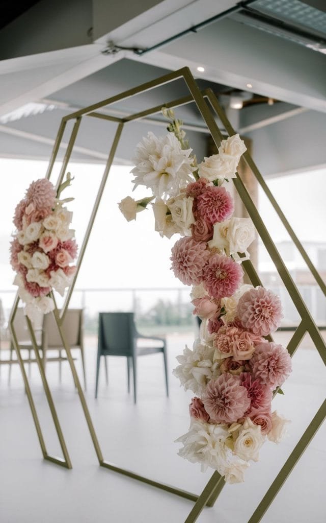 Unique Wedding Arch Flowers in bold geometric shapes, adorned with dahlias and roses in structured arrangements, offering a chic and trendy wedding setting.
